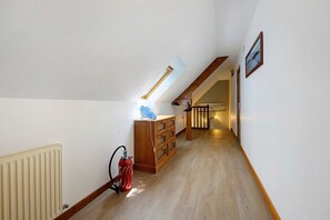 Un pasillo estrecho con suelo de madera, un radiador, un extintor, un armario de madera y una escalera que sube a otro nivel.