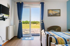 Un dormitorio con cama, televisor, una silla de mimbre y vista a un área verde a través de una puerta corrediza.