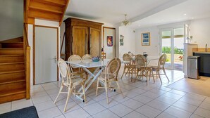 Un espace repas avec une table et des chaises, un coin cuisine équipé d’un réfrigérateur, et un escalier menant à un autre niveau.