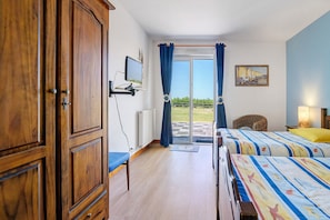 A bedroom with two beds, a wooden wardrobe, a television, and a view of the outdoors. - “Vol de mouettes” Guest Room with Shared Garden and Wi-Fi (Huisnes-sur-Mer)