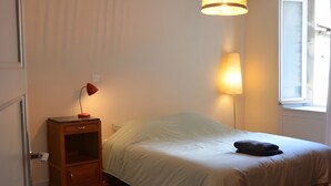 A bedroom with a bed, a bedside table with a lamp, a hanging light fixture, and a window. - Farmhouse Gîte - "La Popote" (Passenans)