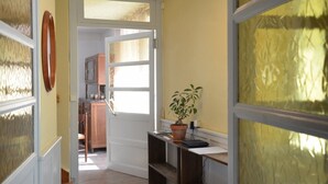 A hallway with a wooden door, a potted plant, and a view into a kitchen area. - Farmhouse Gîte - "La Popote" (Passenans)