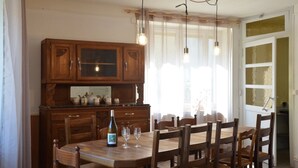A dining area with a wooden table and chairs, a cabinet with glass doors, and hanging pendant lights. - Farmhouse Gîte - "La Popote" (Passenans)