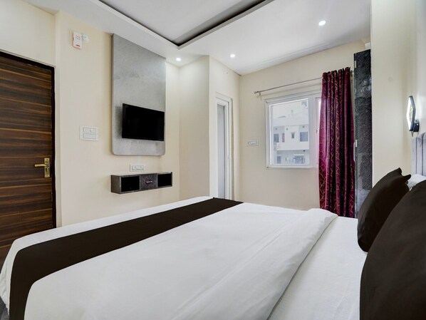 A hotel room with a bed, a mounted TV, a window with curtains, and a door. - Collection O IIT BHU Singh Residency (Varanasi)