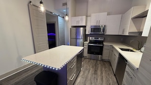 Cocina moderna con isla central, electrodomésticos de acero inoxidable y suelo de madera gris.