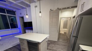 Una cocina moderna con una isla central, electrodomésticos de acero inoxidable y un acceso corredizo a un baño.