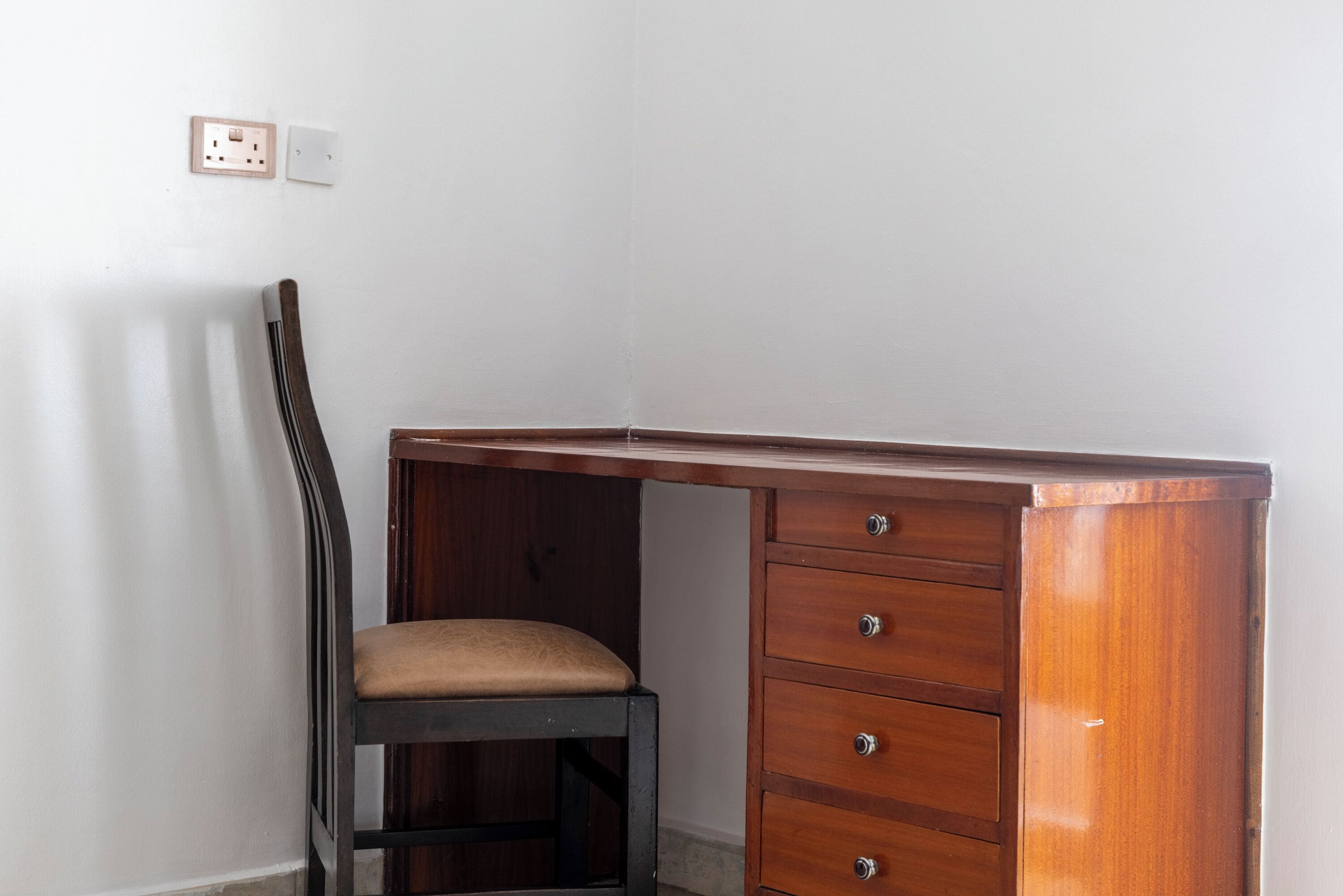 Un bureau d’angle avec une chaise, un tiroir et un interrupteur sur le mur.