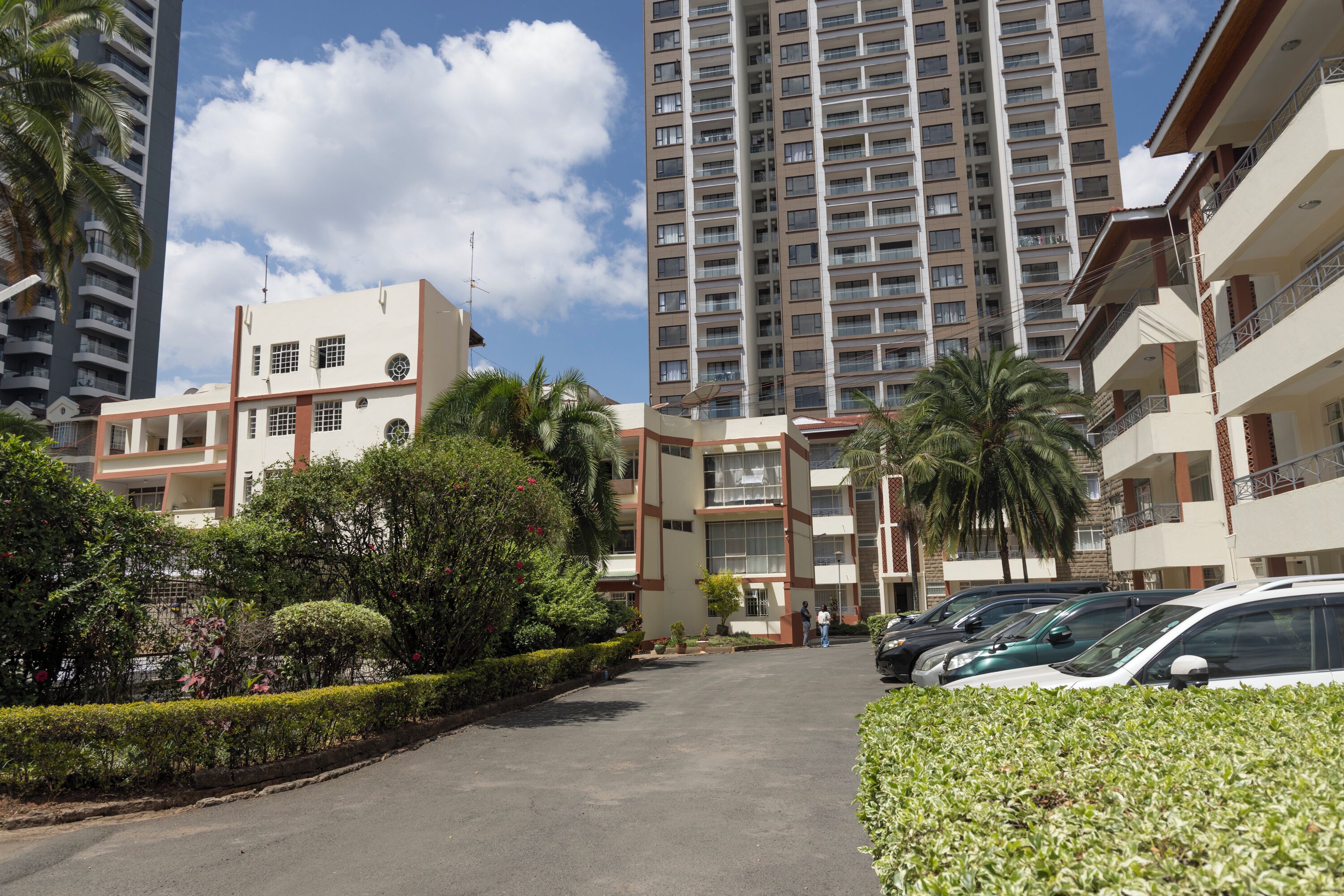 A residential area with modern apartment buildings, a parking lot, and well-maintained greenery.