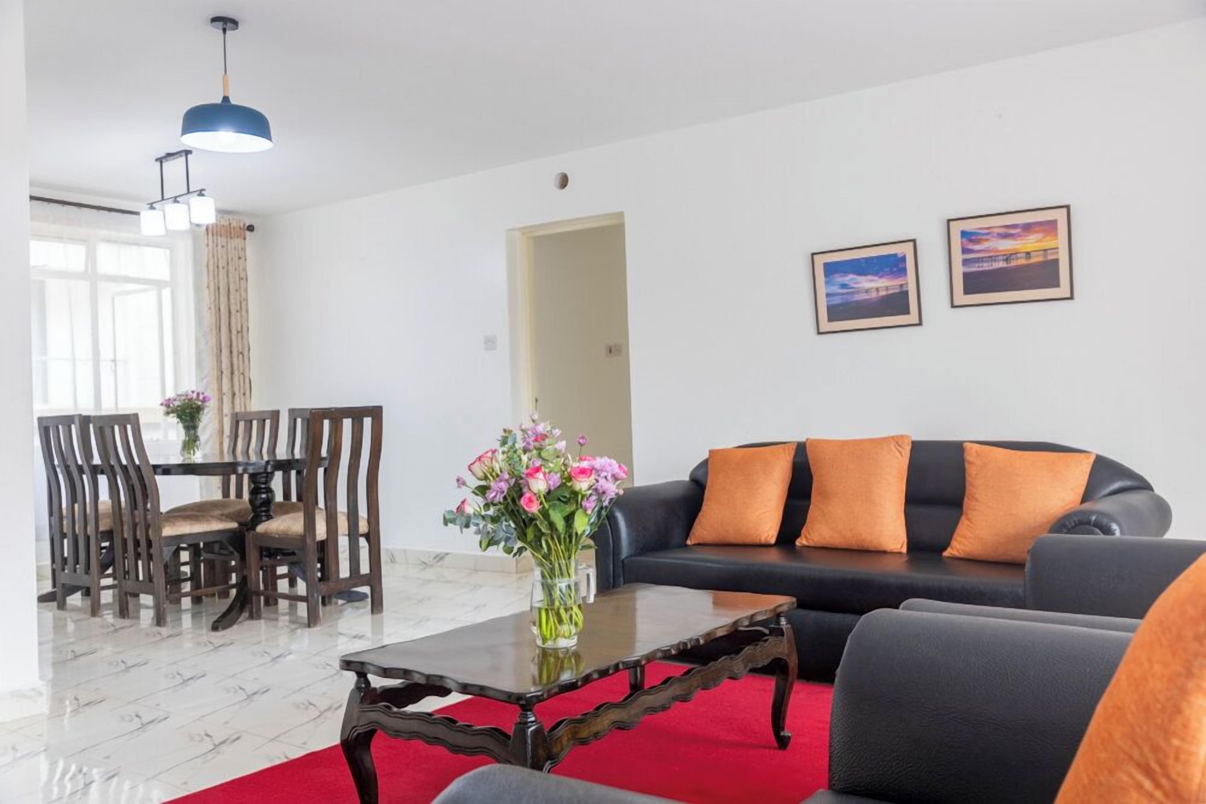 A modern living room with a black sofa, wooden dining table, and chairs. There is a vase with flowers on a coffee table.