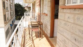 Un balcon avec une table et des chaises, une vue sur le paysage urbain et un immeuble à la façade en pierre.