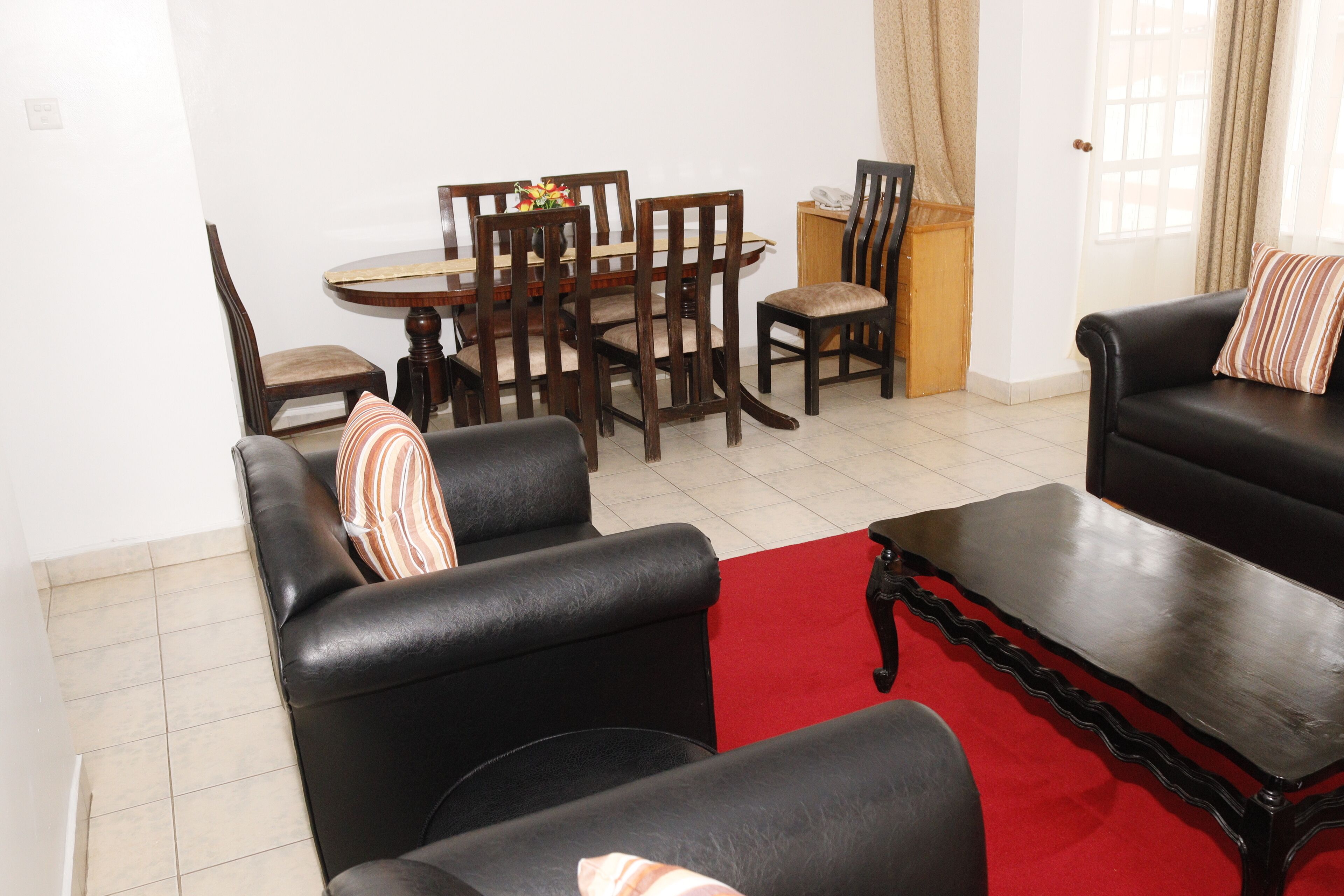 A living room with a red carpet, black leather sofas, wooden dining table, and chairs.