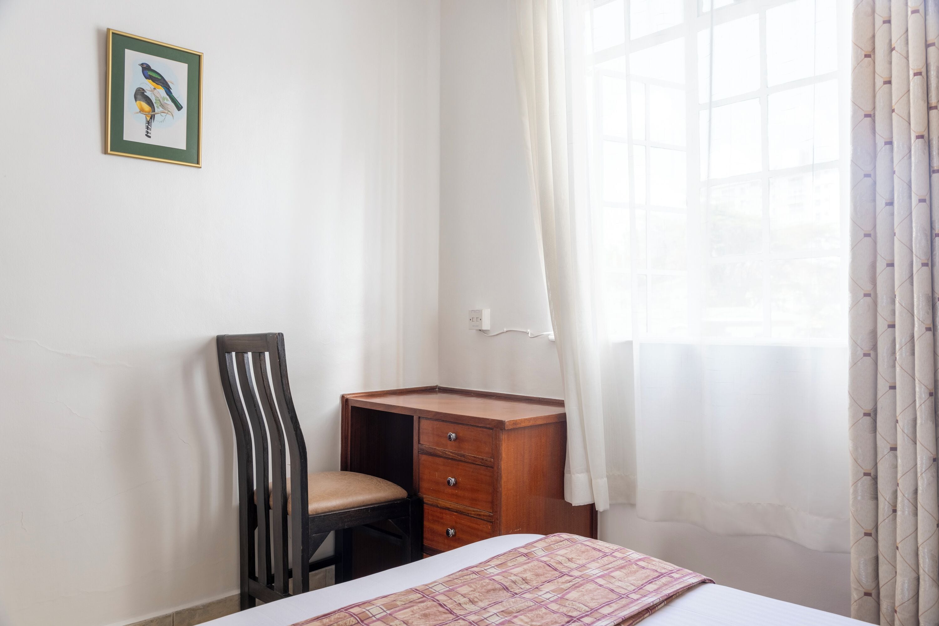 A bedroom with a single bed, a wooden desk, a chair, and a window with curtains.