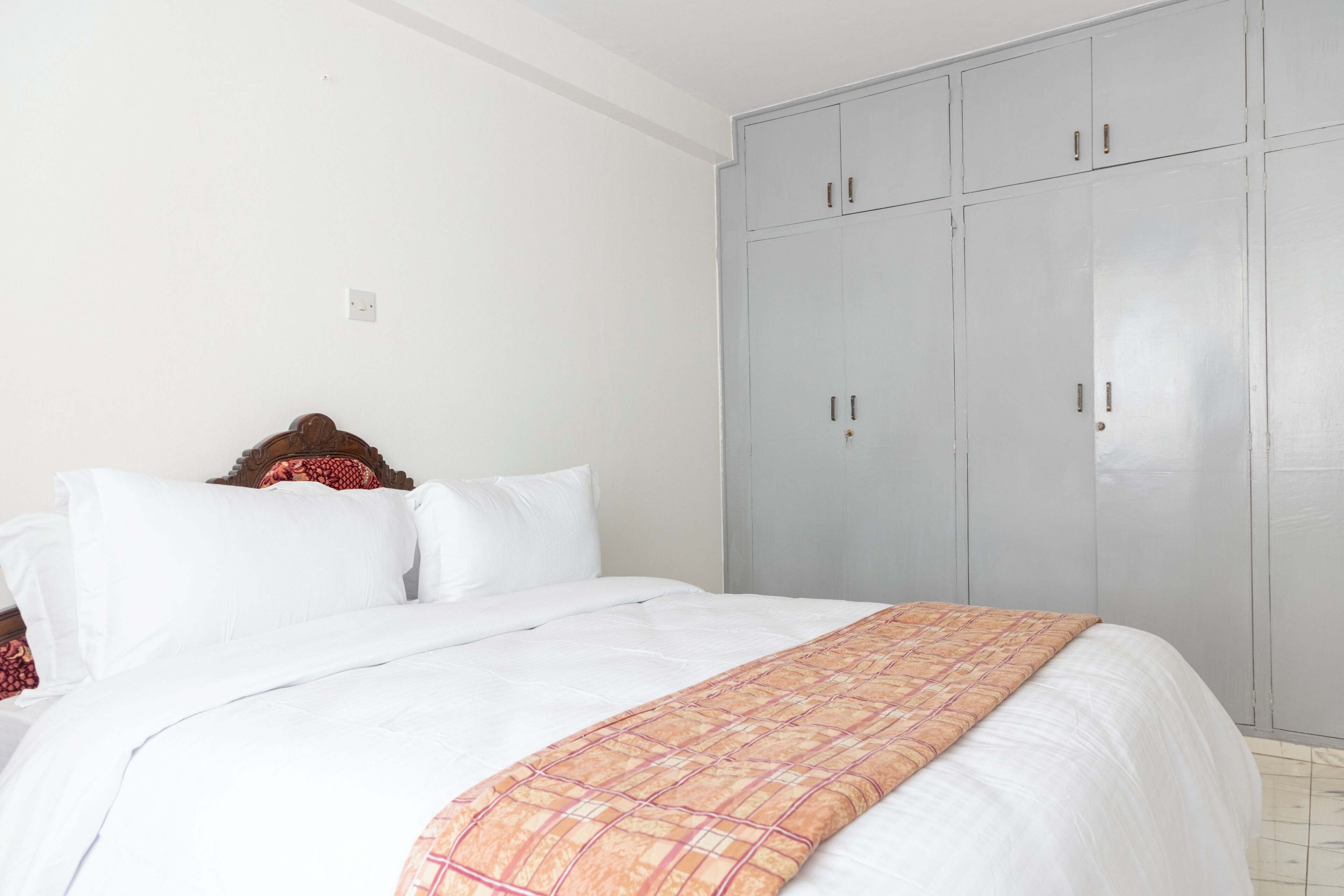A bedroom with a bed, white bedding, a patterned blanket, and a grey wardrobe.