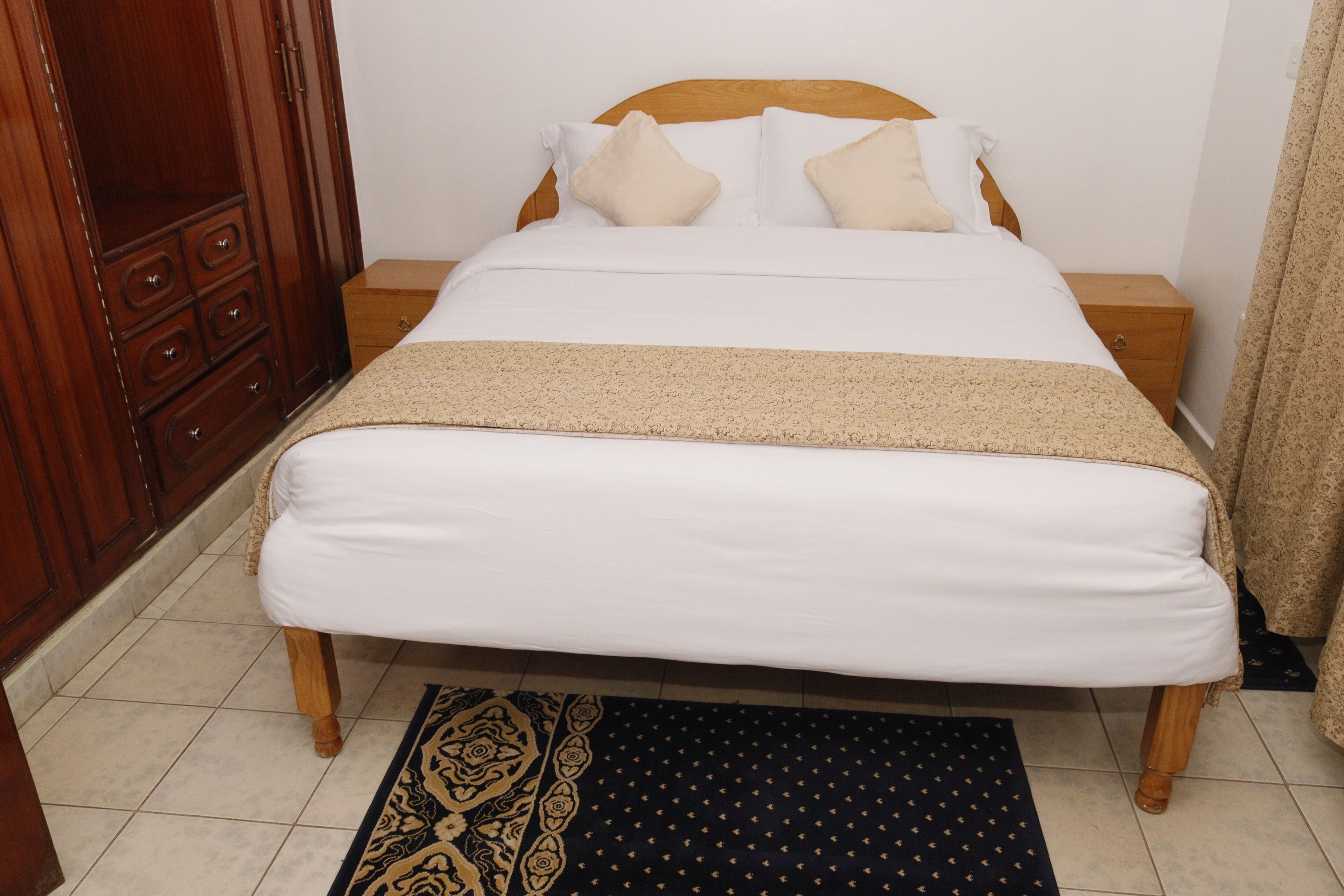 A bed with white bedding, a wooden headboard, and a patterned throw blanket.