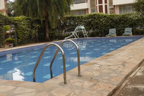 A swimming pool with metal ladders, stone tiles, and a palm tree in the background. - Gemina Court  (Nairobi)