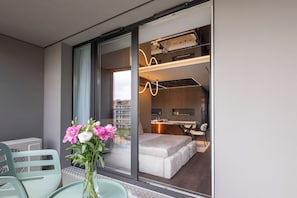 A modern hotel room with a sliding glass door, a dining area with a table and chairs, and a bed with a white headboard. - Native Apartments Wita Stwosza 24 (Kraków)