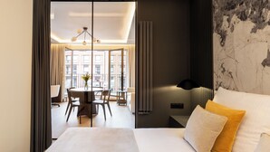 Ein Hotelzimmer mit einem Bett, einem Essbereich mit Stühlen und einem Tisch sowie Blick auf die Stadt durch große Fenster.
