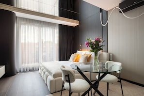 A modern hotel room with a bed, a glass dining table, two chairs, a vase with flowers, and a large window with curtains. - Native Apartments Wita Stwosza 24 (Kraków)