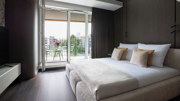 Ein modernes Hotelzimmer mit einem großen Bett, einem Fernseher, einem Balkon mit Stadtblick und einem Essbereich.
