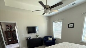 A bedroom with a bed, a ceiling fan, a TV, a dresser, and a window.