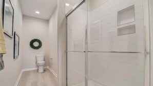 A bathroom with a toilet, a glass shower enclosure, and a wreath on the wall.