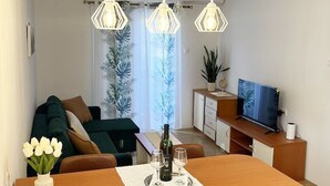 Ein modernes Wohnzimmer mit Esstisch, Sofa, Fernseher und Zimmerpflanzen.