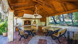 Eine Terrasse im Freien mit Holztischen und -bänken, einem Steinkamin und einer hängenden Leuchte.