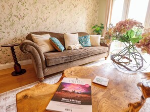 A cozy living room with a brown sofa, decorative pillows, a wooden coffee table with a book, and a vase with flowers. - Rowan Cottage (Boston)