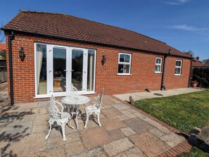 A brick house with a tiled roof, a patio with a table and chairs, and a small garden. - Rowan Cottage (Boston)