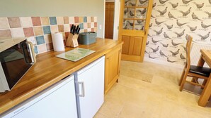 Una cucina con piano di lavoro in legno, frigorifero bianco, zoccolo schienale piastrellato e una porta decorata con un motivo a gallina.