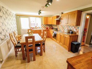 A kitchen with wooden cabinets, a tiled backsplash, a dining table with chairs, and a window with curtains. - Rowan Cottage (Boston)