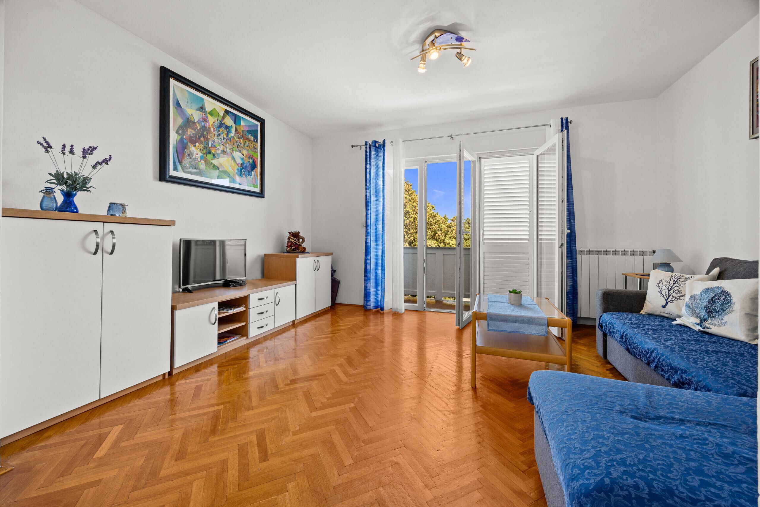A modern room with a wooden floor, a sofa, a TV, a cabinet, and a painting on the wall.