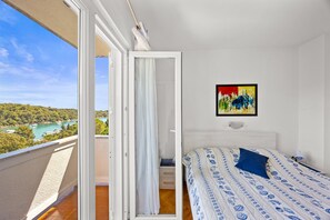 A bedroom with a bed, a painting, and a view of a lake and trees. - Petra Sea View Apartment 4 (Kampor)