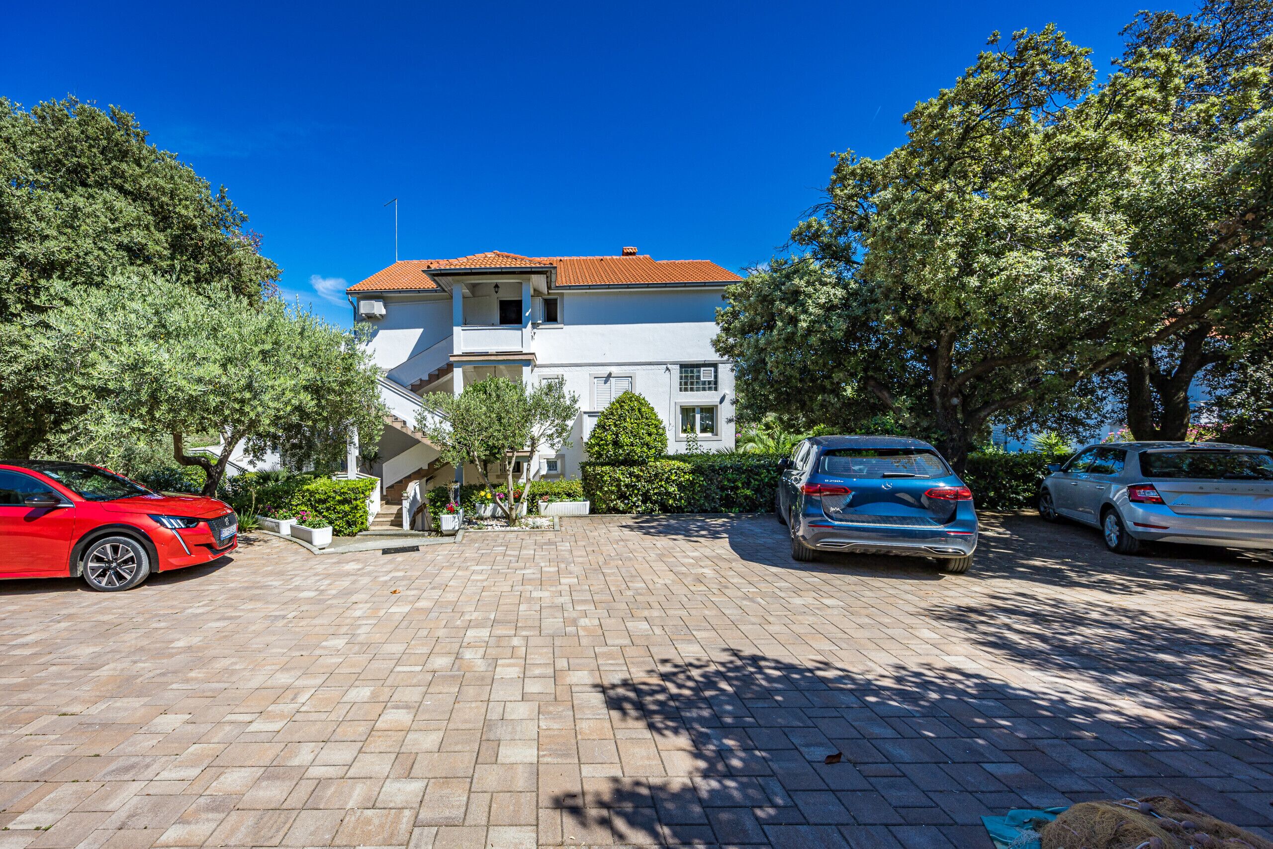 A two-story building with a red-tiled roof, a paved driveway, and parked cars.