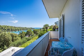 A balcony with a table and chairs, overlooking a coastal landscape with trees and a body of water. - Petra Sea View Apartment 4 (Kampor)
