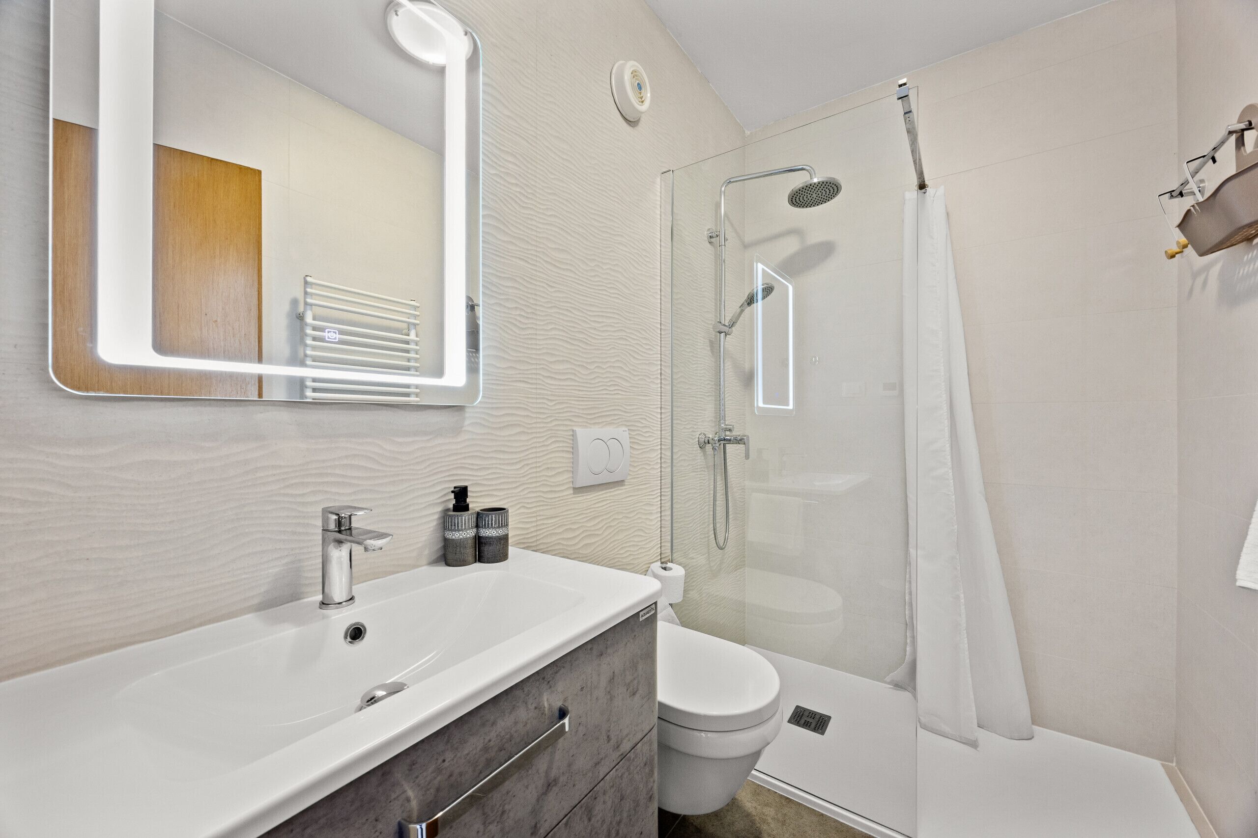 Un baño moderno con lavamanos, espejo y ducha blancos.