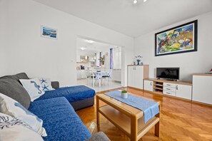 A modern living room with a sofa, a coffee table, a TV, and a kitchen in the background. - Petra Sea View Apartment 4 (Kampor)