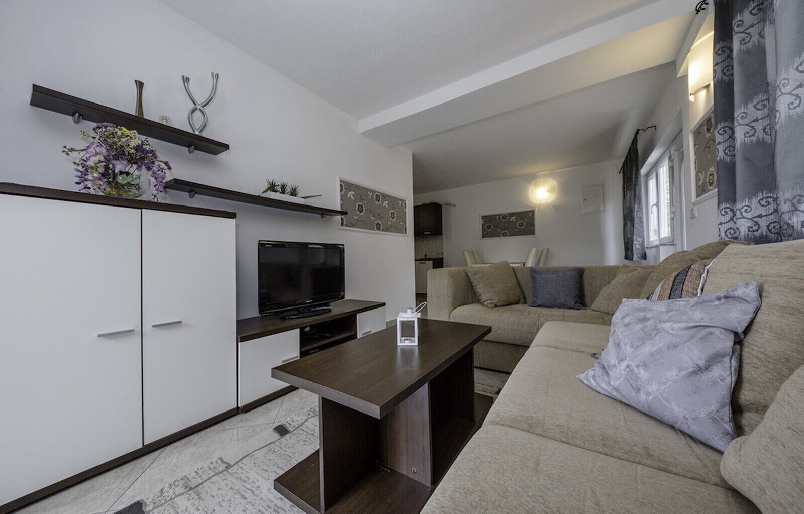 A modern living room with a flat-screen TV, a sofa, a coffee table, and a kitchen area in the background.