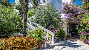 Un edificio con facciata in pietra, un balcone e un'area d'ingresso pavimentata con piante in vaso.
