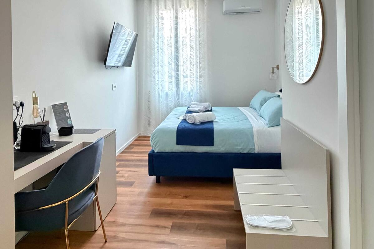 A modern hotel room with a bed, desk, chair, and a TV mounted on the wall.