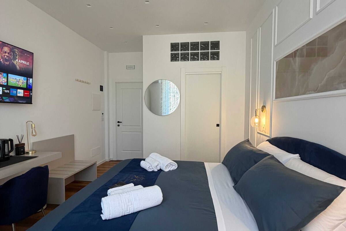 A modern hotel room with a bed, a desk, a TV, and a circular mirror.