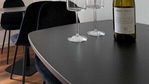 Een tafel met een wijnfles en twee glazen in een kamer met witte muren en zwarte stoelen.