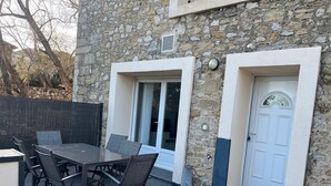 Eine Terrasse im Freien mit Tisch und Stühlen, einer Steinmauer und einer Tür.