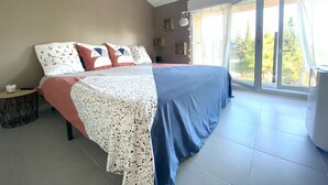 Ein Schlafzimmer mit Bett, Nachttisch, Lampe und Blick ins Freie.