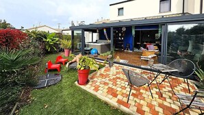 A modern house with a patio, outdoor seating, and a glass door leading to a covered area. - A l'ombre des 2 tilleuls (Sainte-Pazanne)