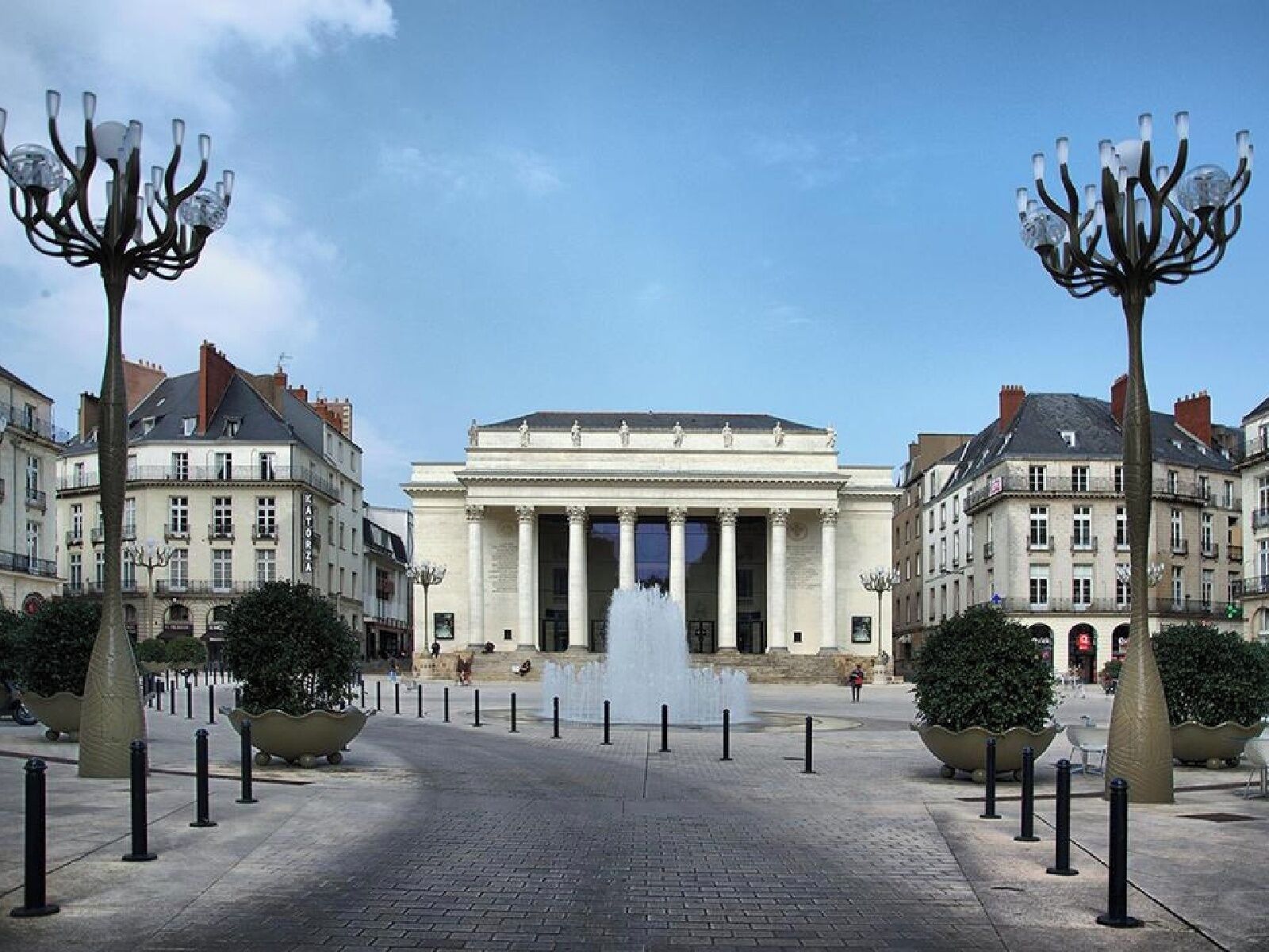 Un imponente edificio con architettura classica, una fontana centrale e lampioni simmetrici.