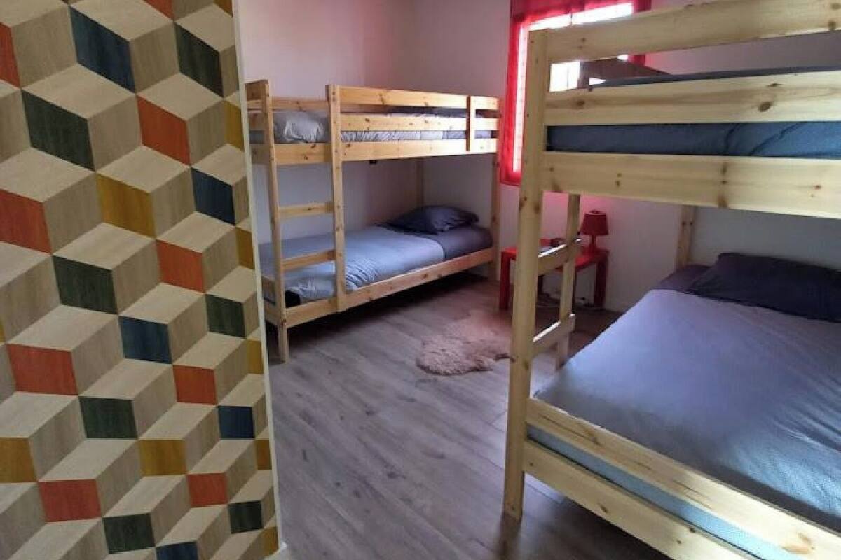 A room with two bunk beds, a small table, a lamp, and a geometric-patterned wall.