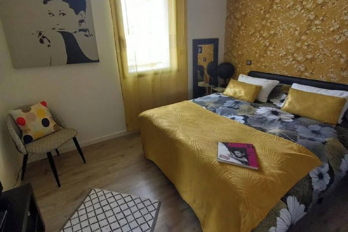 A bedroom with a bed, a chair, a window, and a wall with a floral pattern.