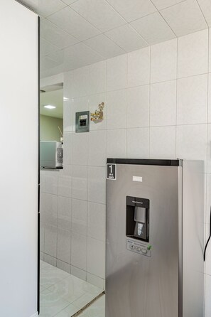 Eine moderne Küche mit einem Edelstahl-Kühlschrank, einem Wasserspender und einem kleinen Stromverteiler an der Wand.
