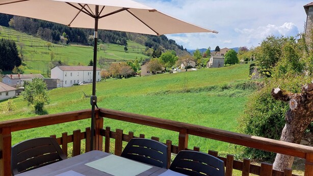 Eine Terrasse mit Tisch und Stühlen, einem Sonnenschirm und Blick auf eine grüne Landschaft.